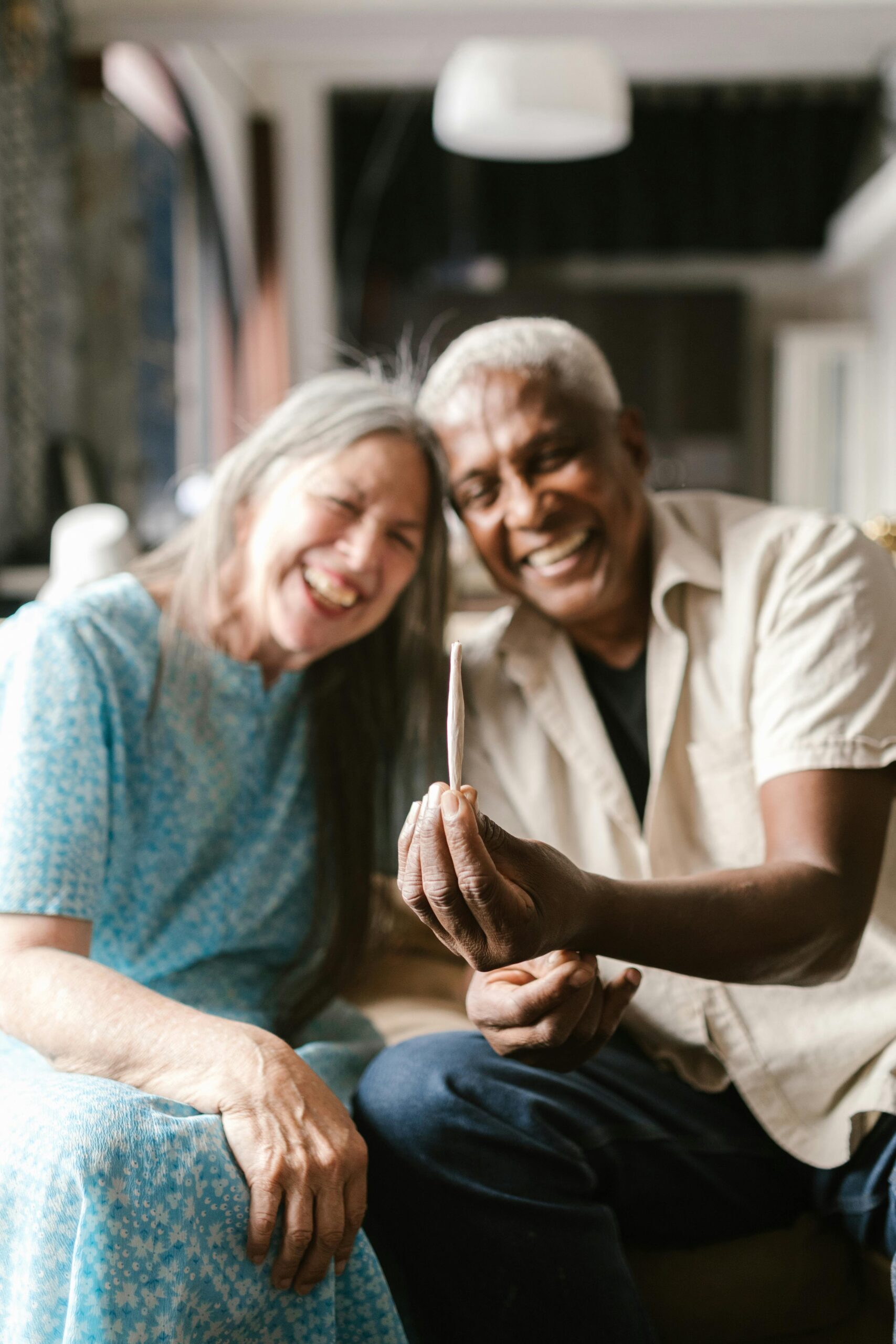 Happy senior couple smiling while holding a joint in a cozy living room setting.